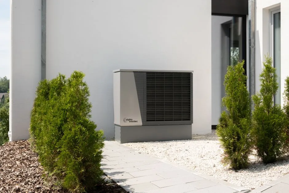 Unité extérieure de pompe à chaleur installée contre une façade, entourée de verdure
